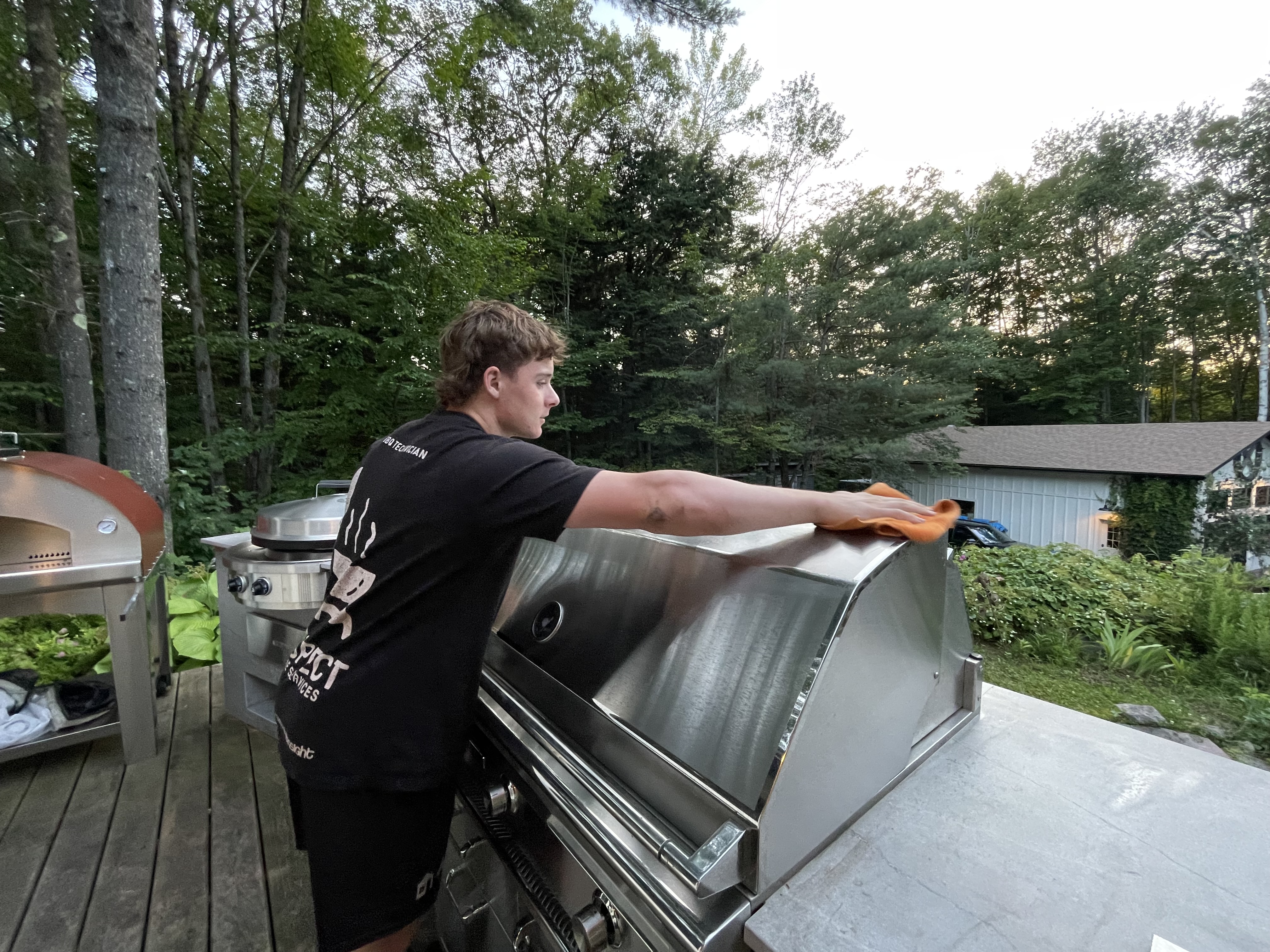 Aspect tech wiping down a stainless BBQ at a cottage at golden hour